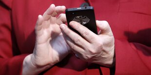 Angela Merkel hält ein Smartphone mit Bundesadler in der Hand