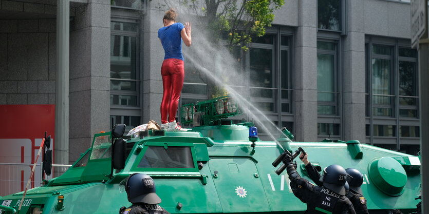 Zwei Polizisten sprühen mit Pfefferspray auf eine Demonstrantin, die auf einem Polizeipanzer steht