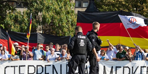 Demonstranten mit Transparent "Sterben, Frau Merkel", davor Polizisten