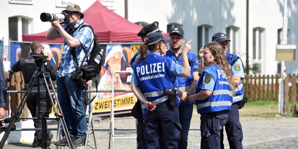 Eine Gruppe Polizisten steht neben einem Mann, der mit einer großen Kamera auf einer Leiter steht und ein Foto schießt