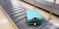 Ein türkiser Koffer auf dem Gepäckband am Flughafen