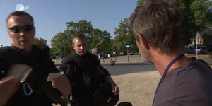 Zwei Polizisten und ein Mann stehen sich gegenüber