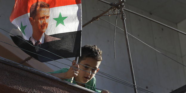 Ein syrischer Junge schwenkt in Damaskus eine zerrissene Assad-Fahne