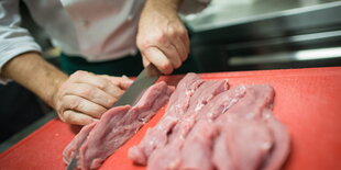 Jemand steht hinter einem roten Brett, auf dem drei Stücke Fleisch liegen