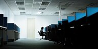 Ein Mann sitzt einsam am Ende einer Reihe von Arbeitsplatznischen in einem Großraumbüro