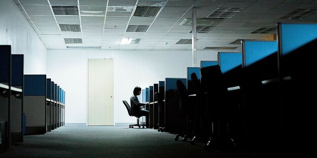 Ein Mann sitzt einsam am Ende einer Reihe von Arbeitsplatznischen in einem Großraumbüro