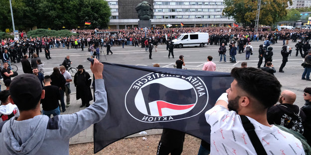 Menschen mit einer Antifa-Flagge stehen auf der gegenüberliegenden Straßenseite von einer großen Menschenmenge