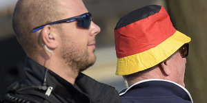 Mann mit Sonnenbrille und Headset neben Mann mit schwarz-rot-goldenem Hut