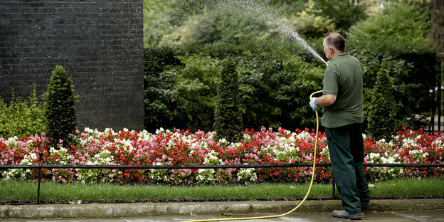 Ein Mann gießt Blumen mit einem Gartenschlauch