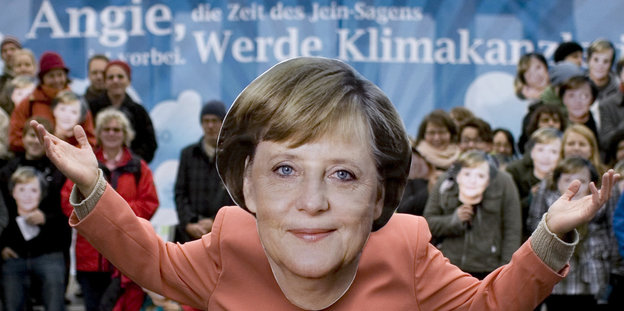 Aktivisten verkleidet als Angela Merkel vor dem Plakat mit der Aufschrift "Angie, werde Klimakanzlerin"