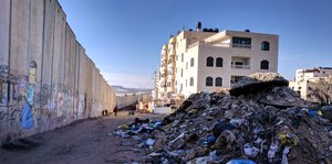Die israelische Trennmauer vor blauben Himmer, im Hintergrund Gebäude, im Vordergrund ein Müllberg.