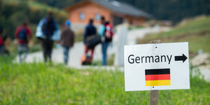 Flüchtlinge aus Syrien gehen nahe der deutschen Grenze hinter einem Schild mit der Aufschrift "Germany" und der Abbildung einer deutschen Fahne einen Weg entlang
