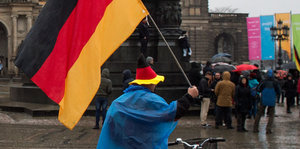 Bei Pegida in Dresden steht ein Mann mit Deutschlandhut und Deutschlandfahne