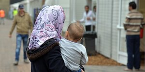 Eine Kopftuch tragende Frau hält ein Kind auf dem Arm; im Hintergrund Männer