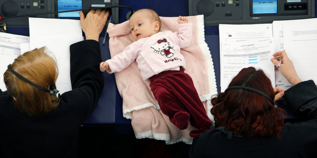Im EU-Parlament liegt ein Baby zwischen zwei Frauen auf einem Tisch