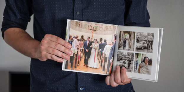 Ein Mann zeigt ein Fotobuch mit Fotos seiner Hochzeit. Die Braut war in Weiß