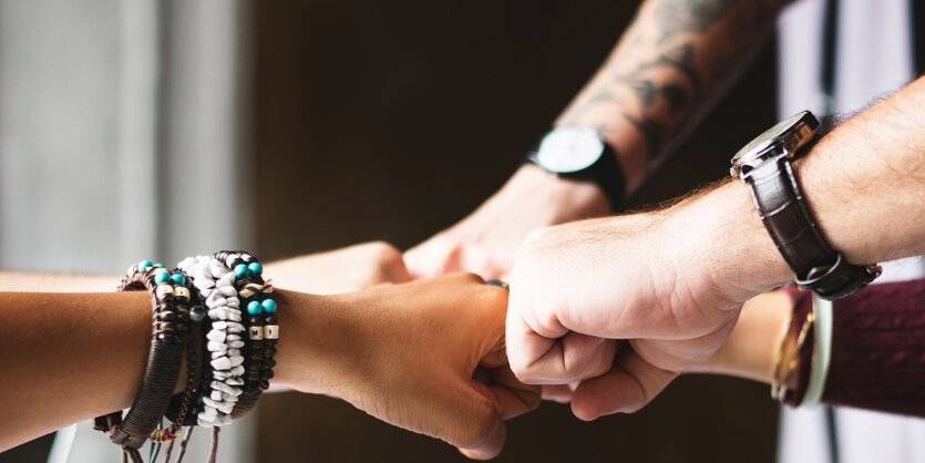 Vier Menschen geben sich die Faust und tragen Armbanduhren