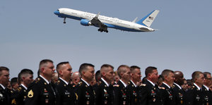 Menschen in Uniform stehen im Vordergrund des Fotos, im Hintergrund ist ein Flugzeug vor blauem Himmel zu sehen.