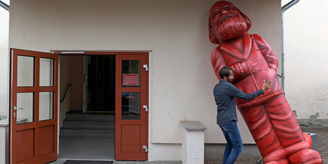 Ein Mann hält eine übergroße Marx-Figur in der Schräge