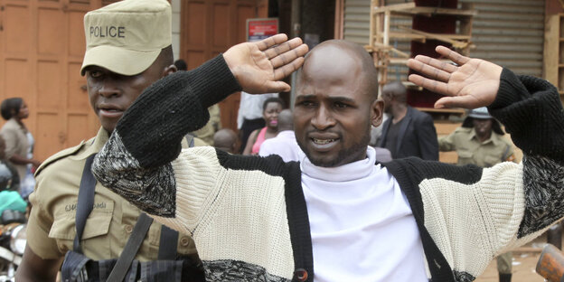 In Uganda führt ein uniformierter Mann einen Mann mit erhobenen Händen ab