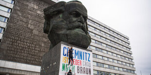 Zwei Männer befestigen am Karl-Marx-Denkmal ein Plakat mit der Aufschrift "Chemnitz ist weder grau noch braun".