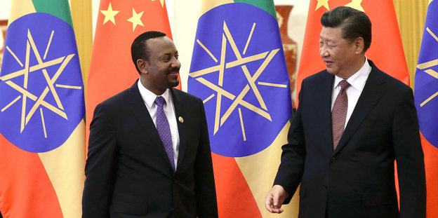 Im Hintergrund bunte Flaggen, im Vordergrund zwei Männer: Abiy Ahmed aus Äthiopien und Xi Jinping aus China. Beide tragen Anzüge und Krawatten