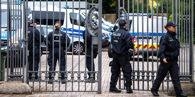 Fünf Polizisten stehen an einem eisernen Tor