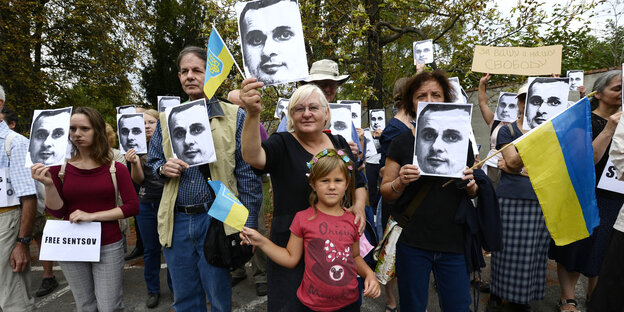 AktivistInnen halten Schilder mit dem Kopf von Oleh Senzow hoch und zeigen ukrainische Nationalflaggen