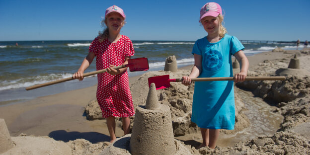 Zwei kleine Mädchen bauen eine Sandburg.