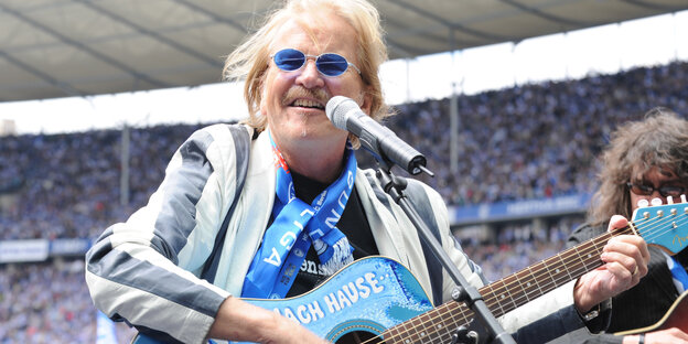 Frank Zander mit blauer Sonnenbrille, Hertha-Schal und blauer Gitarre im Stadion