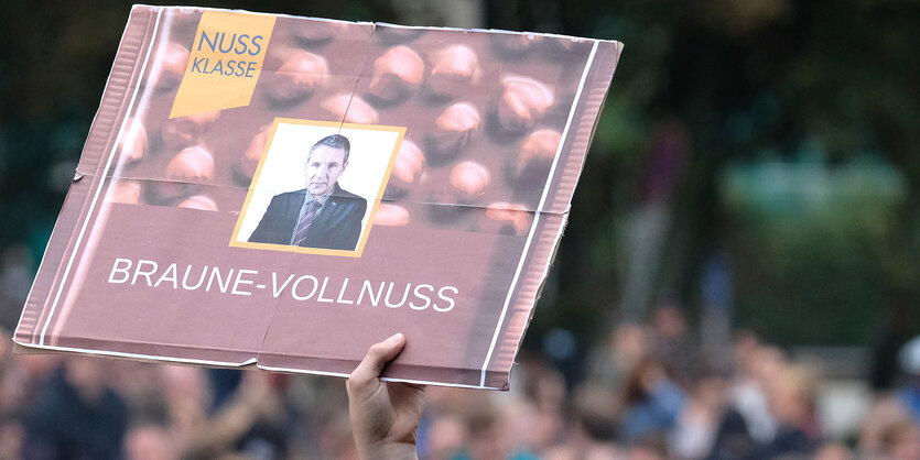 Aus einer Menschenmenge wird ein Plakat im Stil einer Schokoladenpackung und mit der Aufschrift „Braune Vollnuss“ gezeigt