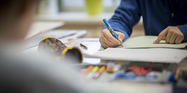 Bildungspaket: Ein Schüler schreibt mit Füller auf ein Blatt, vor ihm liegen unter anderem ein Etui und mehrere Stifte. Bildungspaket: Ein Schüler schreibt mit Füller auf ein Blatt, vor ihm liegen unter anderem ein Etui und mehrere Stifte.