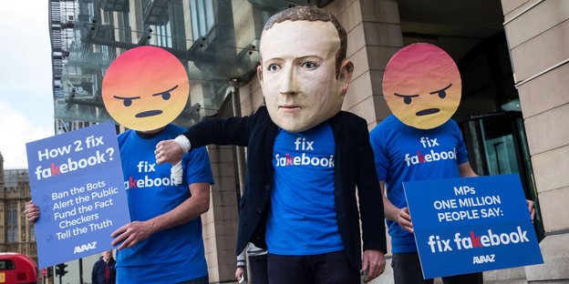 Verkleidete Aktivisten mit Emojis und Zuckerberg-Maske protestieren gegen Fake News auf Facebook