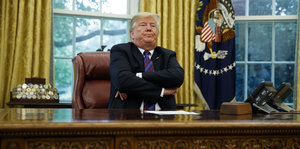Donald Trump mit verschränkten Armen am Schreibtisch im Oval Office