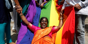 Eine Frau liegt glücklich auf einer Regenbogenflagge und wird von anderen Personen festgehalten