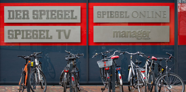 Fahrräder stehen an Fahrradständern. Dahinter die Schriftzüge. Der Spiegel, Spiegel TV, Spiegel Online und Manager Magazin