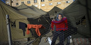 Frau steht vor Wohnzelten und hängt Wäsche über einen Zaun
