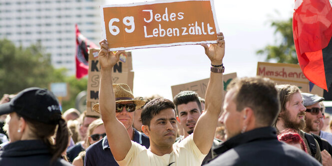 Ein Mann hält auf einer Demo ein Schild hoch, darauf steht 
