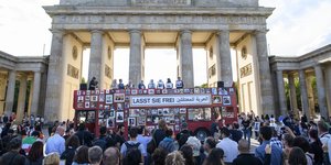 Ein roter Bus, mit gerahmten Fotos behangen, steht vor dem Brandenburger Tor
