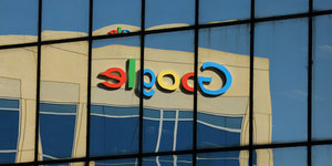 Ein Google-Logo, das an einer Fassade angebracht ist, spiegelt sich in einer Glasfassade