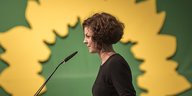 Gesine Agena ist im Profil zu sehen, sie steht an einem Rednerpult vor dem Sonnenblumen-Logo der Grünen