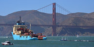 An der Golden Gate Bridge von San Francisco schleppt ein Schiff ein langes Rohr hinter sich her