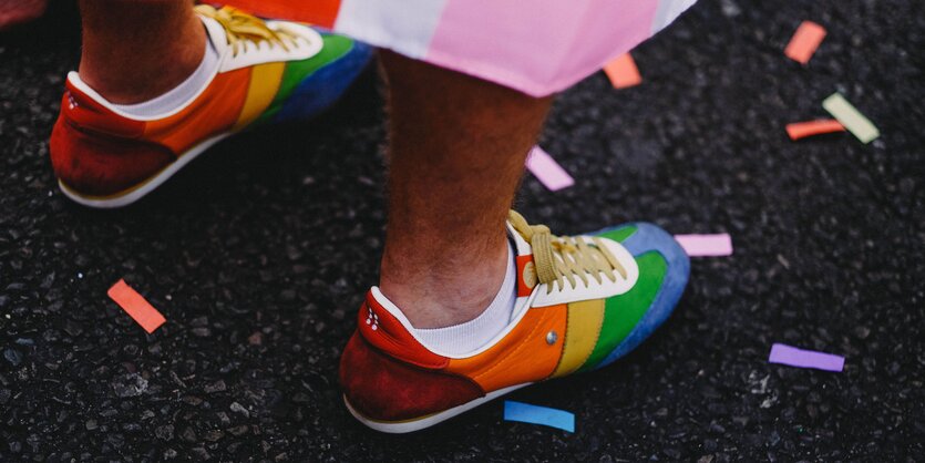 Zwei Regenbogenfarbige Turnschuhe auf grauem Asphalt