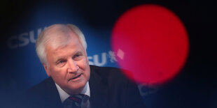 Horst Seehofer sitzt hinter einem runden, roten Lichtreflex