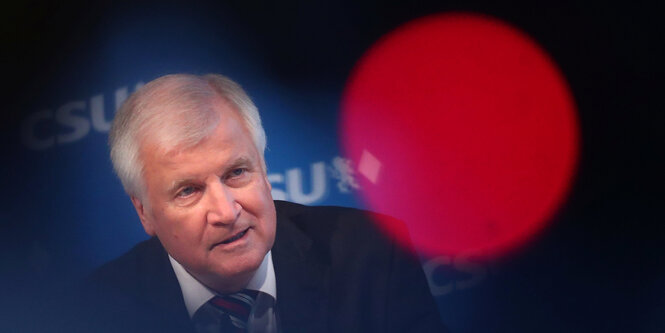 Horst Seehofer sitzt hinter einem runden, roten Lichtreflex