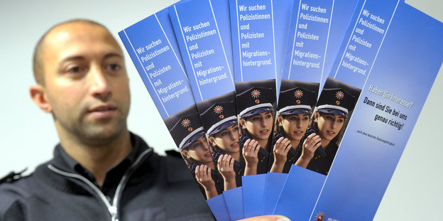 Ein Polizist zeigt Werbebroschüren, die sich an Nachwuchspolizisten mit Migrationshintergrund wenden.