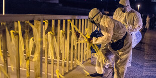 Zwei Menschen in Schutzanzügen ziehen an Papierbändern, die an einer Brücke festgebunden sind