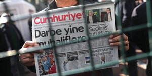 Jemand hält eine Ausgave von Cumhuriyet hinter einem Gitter hoch