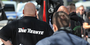 Ein glatzköpfiger Mann mit einem schwarzen T-Shirt, auf dem das Logo der Partei "Die Rechte" abgebildet ist.
