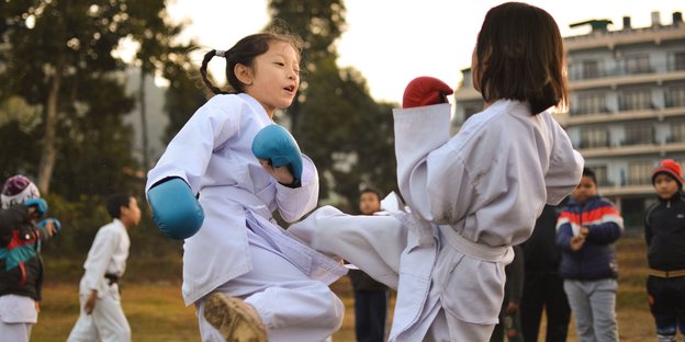 Zwei Mädchen kämpfen Judo mit Boxhandschuhen und weißen Kampfsport-Anzügen gegeneinander Zwei Mädchen kämpfen Judo mit Boxhandschuhen und weißen Kampfsport-Anzügen gegeneinander